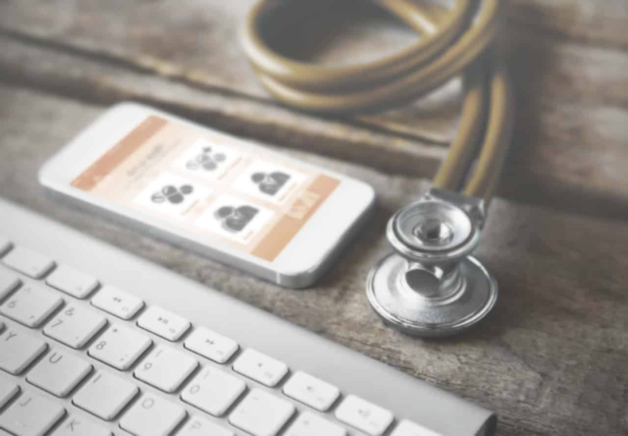 Smartphone liegt vor einer Tastatur, auf dem Screen ist die Patientenverwaltung & Arztsoftware von 4myHEALTH zu sehen, daneben liegt ein Stethoskop